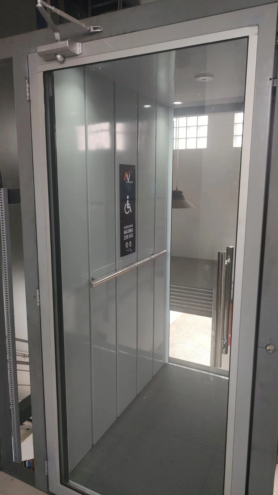 Elevador com portas de vidro e cabine cinza em ambiente comercial